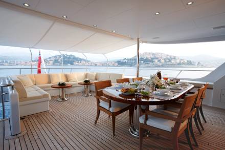 An elegant yacht deck offers a picturesque dining setting with a view of a charming coastal town.