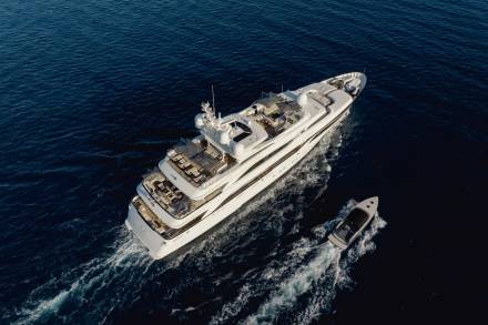 A luxurious white yacht cruises through deep blue waters, trailed by a smaller tender boat.