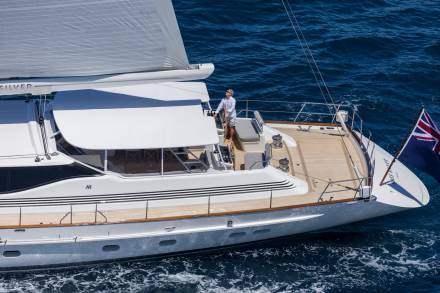 A man steers a luxurious yacht through the deep blue ocean under a bright sky.