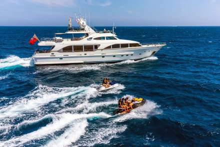 Jet skiers race alongside a luxurious yacht on a bright, sunny day at sea.