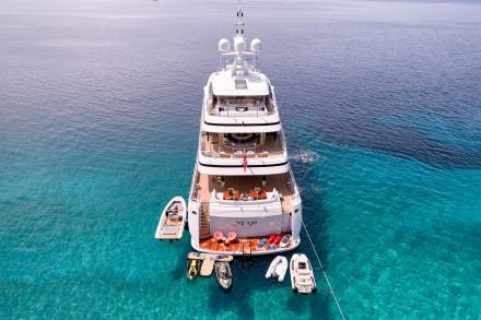 A luxurious superyacht rests in crystal-clear turquoise waters, surrounded by an array of watercraft ready for adventure.