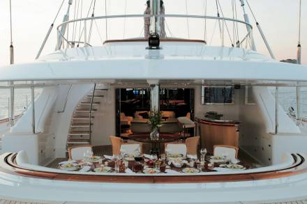 A beautifully set dining table awaits guests on the deck of a luxurious yacht, ready for an al fresco meal at sea.