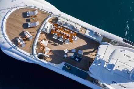 An aerial view reveals a luxurious yacht's deck set for a grand outdoor dining experience amidst the tranquil blue sea.