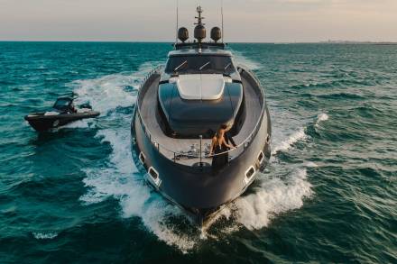 A sleek yacht cuts through the turquoise waves, accompanied by a smaller tender boat, as a couple enjoys the open sea.