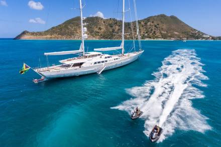 Two jet skiers race across the turquoise waters, leaving a foamy wake behind a majestic white yacht anchored near a tropical island.