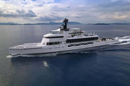 The luxurious yacht Wanderlust glides through calm blue waters with a mountainous coastline in the distance.
