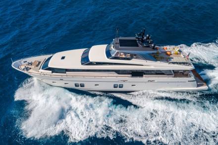 A sleek white yacht glides through the deep blue ocean, leaving a trail of white foam in its wake.