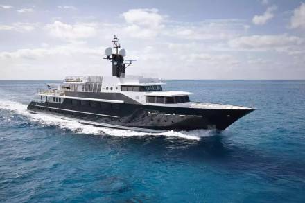 A sleek black and white yacht glides through the vibrant blue ocean under a cloudy sky.