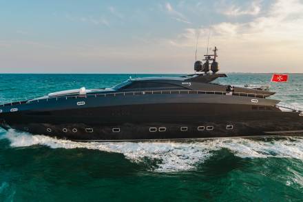 A sleek black yacht cuts through the turquoise ocean waves under a pale sky.