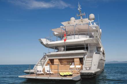 A large, luxurious yacht with multiple decks and a sleek, modern design sits on the calm, blue waters of the ocean, surrounded by a clear, cloudless sky.
