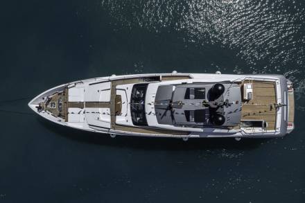 An elegant white yacht glides through the shimmering dark blue water under a bright sun.