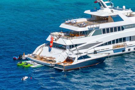 A luxurious superyacht named "Rockit" is anchored in clear blue waters, surrounded by various watercraft.