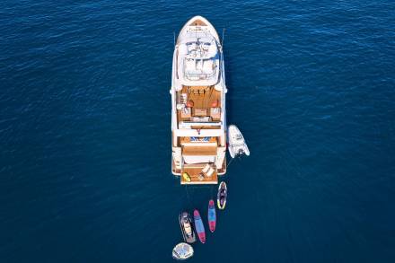 A luxurious yacht floats serenely on the deep blue sea, surrounded by inflatable water toys and paddleboards.