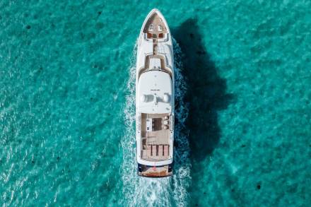 A luxurious white yacht glides through crystal-clear turquoise waters, leaving a foamy wake behind.