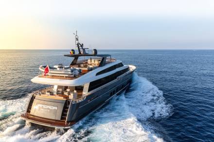 A sleek, modern yacht cruises through the deep blue sea, leaving a foamy wake under a warm, golden sky.