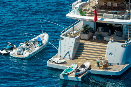 A luxurious yacht is moored in the azure sea, with a tender, jet skis, and paddleboards ready for adventure.