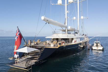A large, luxurious sailing yacht with a British flag floating on the calm, blue ocean waters, surrounded by a serene and picturesque backdrop.