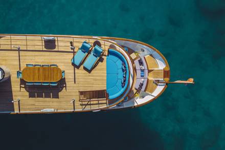 A luxurious yacht with vibrant turquoise cushions and a wooden deck floats serenely in the clear blue ocean.