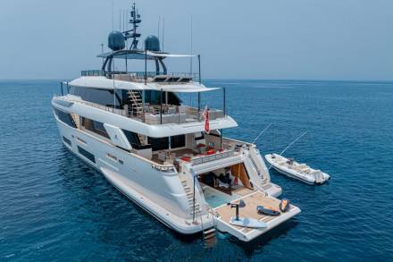 A luxurious superyacht floats serenely on the azure sea, its open aft deck revealing a swimming platform and water toys.