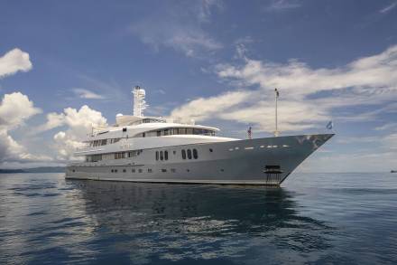 A luxurious yacht named "DREAM" glides serenely across calm waters under a bright, cloudy sky.