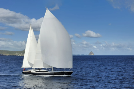 A majestic sailboat glides across the deep blue ocean under a bright, cloud-dotted sky.