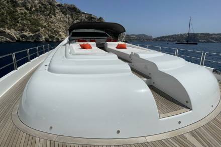 A sleek white yacht with orange cushions rests on the sparkling blue waters of a Mediterranean bay.