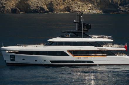 A sleek white yacht named Legend cruises through dark blue waters near a rocky coastline.