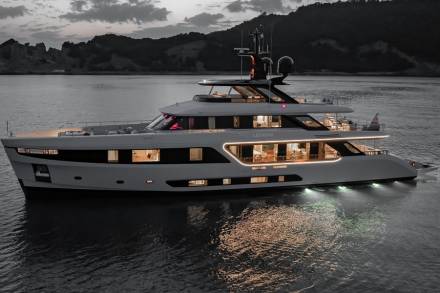A luxurious yacht named Legend glides through calm waters at dusk, its interior lights casting a warm glow.