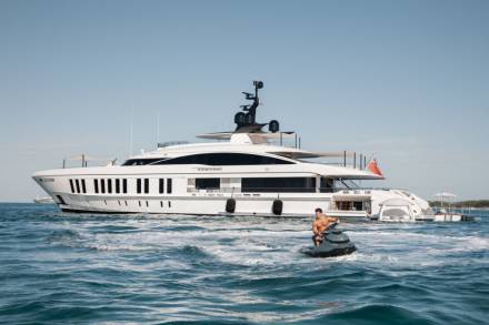 A man enjoys a thrilling ride on a jet ski in front of a luxurious yacht under a clear blue sky.