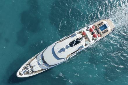 A luxurious yacht glides through the turquoise waters, its decks adorned with red umbrellas and a sparkling swimming pool.