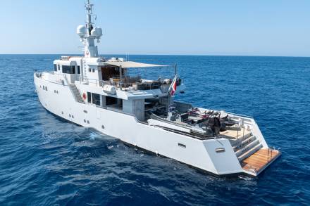 A sleek white yacht cruises on the deep blue sea, carrying jet skis and a tender on its expansive aft deck.