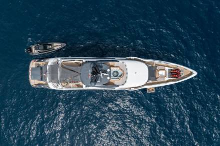 A sleek white yacht with a helipad and jet skis glides through the deep blue ocean, accompanied by a smaller tender boat.