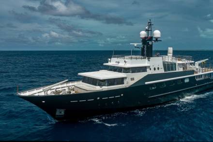 A sleek, dark yacht cuts through the deep blue ocean under a dramatic, cloudy sky.