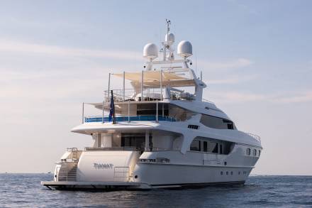 A luxurious white yacht glides across the calm blue sea under a bright, cloudy sky.