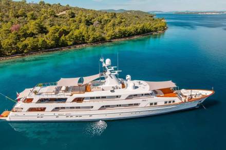 A luxurious white yacht glides through the crystal-clear turquoise waters of a secluded bay, fringed by lush green islands.