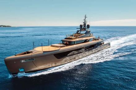 A luxurious bronze yacht glides through the deep blue ocean, leaving a white wake behind it.