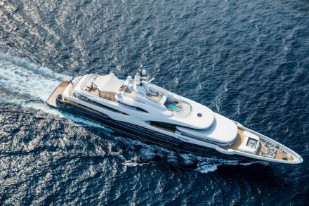 A luxurious superyacht named Barbara glides through the deep blue ocean, leaving a white wake behind.