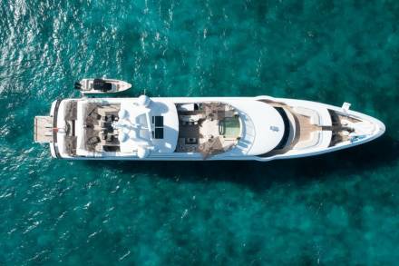 A luxurious yacht floats serenely in crystal-clear turquoise waters, accompanied by a smaller tender boat.