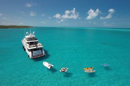 A luxurious yacht anchors in crystal-clear turquoise waters, surrounded by various watercraft for aquatic adventures.