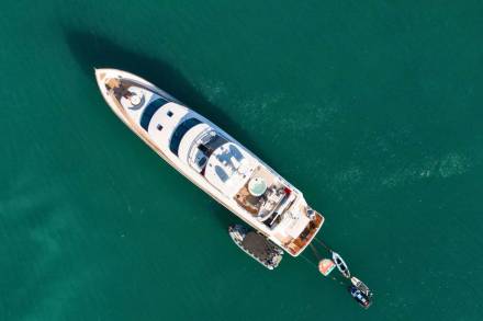 A luxurious yacht floats serenely in the emerald waters, accompanied by its smaller tenders.