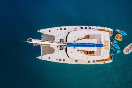 A luxurious catamaran anchors in crystal-clear turquoise waters, surrounded by inflatable toys and a tender boat.