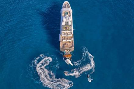 A luxurious yacht floats on the deep blue sea, surrounded by the playful trails of jet skis.