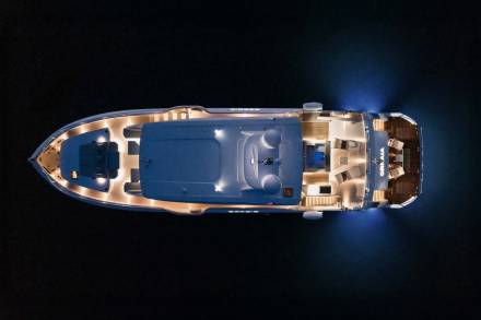 This aerial view captures a luxurious yacht illuminated at night, its interior lights casting a warm glow on the dark water.