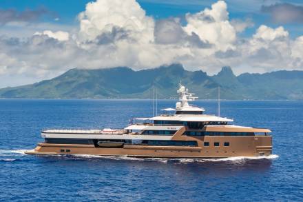 A luxurious yacht cruises through the deep blue waters with lush green mountains in the background.