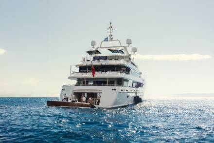 A luxurious superyacht glides across the sparkling blue ocean under a clear sky.