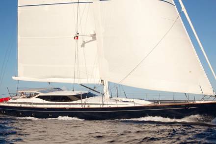 A majestic dark blue yacht glides through choppy blue waters under a vast expanse of white sails.