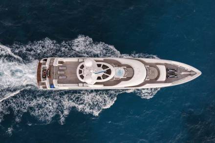 A large white yacht is seen sailing on the deep blue ocean, surrounded by white-capped waves and a clear, starry sky in the background.