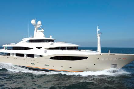 A sleek, modern yacht glides through the azure waters under a clear blue sky.
