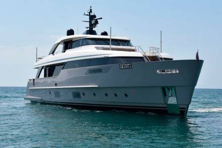 A large, sleek yacht with a distinctive gray hull and white superstructure is seen floating on the calm, blue waters of the ocean against a clear sky.