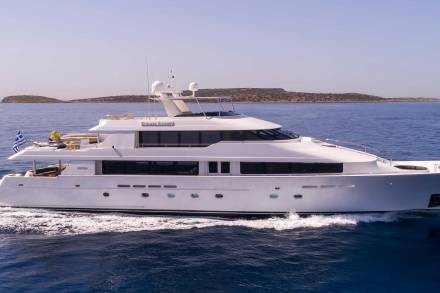 A large white yacht cruises through the deep blue sea, with a distant, rocky island under a clear sky in the background.